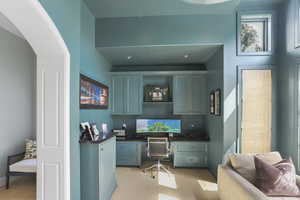 Home office with built in desk, light colored carpet, and arched walkways
