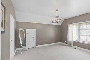 Empty room featuring light colored carpet, a chandelier, and vaulted ceiling