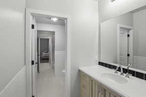 Bathroom with a wainscoted wall, tile walls, vanity, and light tile patterned flooring
