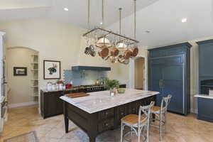 Kitchen featuring arched walkways, light stone countertops, backsplash, a breakfast bar area, and lofted ceiling