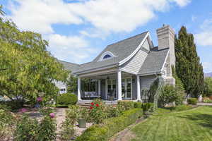 View of front of house featuring roof with shingles, covered porch, a chimney, and a front yard