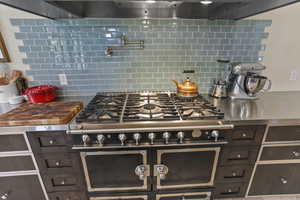 Kitchen view of stainless steel counters, dark brown cabinetry, high end range, pot filler, and wall chimney range hood