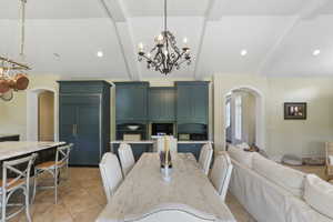 Dining space featuring arched walkways, a chandelier, beam ceiling, light tile patterned floors, and high vaulted ceiling