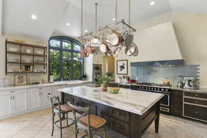 Kitchen with a breakfast bar area, vaulted ceiling, light stone countertops, tasteful backsplash, and light tile patterned floors