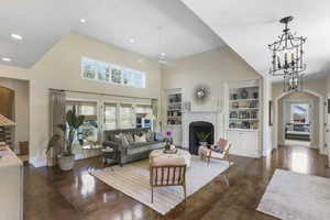 Living room featuring arched walkways, a fireplace with flush hearth, dark wood finished floors, a towering ceiling, and a chandelier
