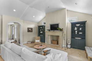 Living room featuring arched walkways, vaulted ceiling, light tile patterned floors, and a high end fireplace