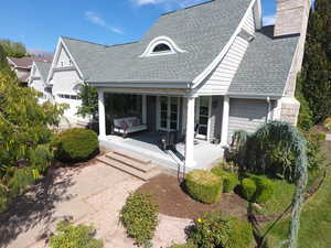 Back of property with a shingled roof, a chimney, and covered porch