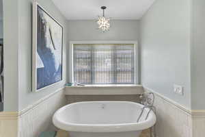Full bath featuring wainscoting, tile walls, and a soaking tub