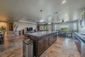Kitchen featuring decorative light fixtures, ceiling fan, dark brown cabinets, light stone countertops, and open floor plan