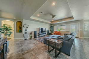 Living area featuring a raised ceiling, ceiling fan, recessed lighting, arched walkways, and a textured ceiling