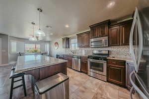 Kitchen with dark brown cabinets, stainless steel appliances, light stone counters, and recessed lighting