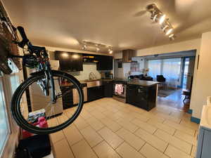 Kitchen featuring dark cabinetry, a peninsula, stainless steel electric range, track lighting, and wall chimney range hood