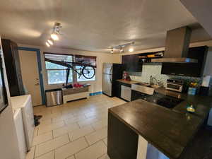 Kitchen featuring a textured ceiling, island exhaust hood, light tile patterned floors, decorative backsplash, and dark cabinets