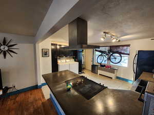 Kitchen featuring freestanding refrigerator, stove, a textured ceiling, island exhaust hood, and independent washer and dryer