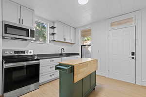 Kitchen featuring stainless steel appliances, quartz countertops, kitchen island, white and green cabinets, and light wood-style flooring