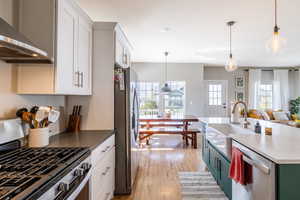 Kitchen with stainless steel appliances, white cabinetry, and wall chimney range hood