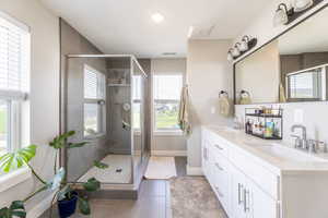 Full bath with double vanity, light tile patterned floors, a shower stall, healthy amount of natural light, and recessed lighting