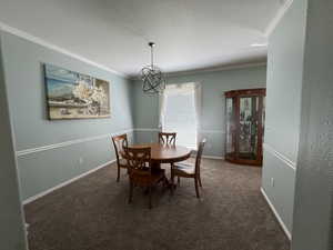 Dining room featuring dark carpet, ornamental molding, a chandelier, and a textured ceiling
