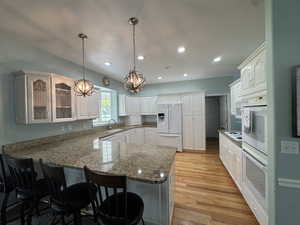 Kitchen featuring white appliances, a breakfast bar, white cabinets, light wood-type flooring, and a peninsula