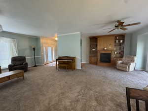 Carpeted living area featuring healthy amount of natural light, crown molding, ceiling fan, a textured ceiling, and a fireplace