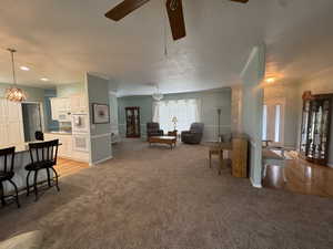 Living area featuring a chandelier, light carpet, a ceiling fan, ornamental molding, and light wood-style floors