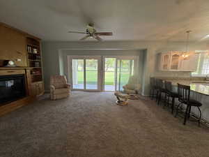 Living area with a glass covered fireplace, carpet, a ceiling fan, a textured ceiling, and a chandelier