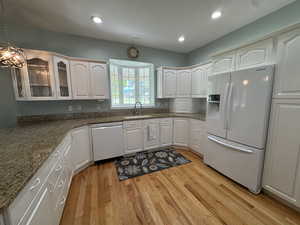 Kitchen featuring white appliances, light wood-type flooring, glass insert cabinets, hanging light fixtures, and white cabinetry
