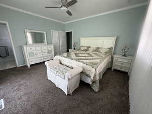 Bedroom with crown molding, a ceiling fan, dark colored carpet, and connected bathroom