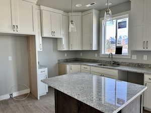 Kitchen with light stone countertops, white cabinets, dark brown cabinets, wood finished floors, and decorative light fixtures