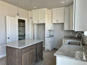 Kitchen with white cabinetry, light stone counters, a center island, wood finished floors, and dark brown cabinets