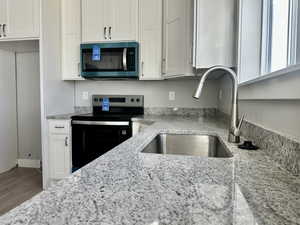 Kitchen featuring stainless steel appliances, white cabinetry, light stone counters, and wood finished floors