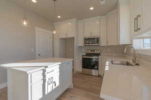 Kitchen featuring stainless steel appliances, white cabinets, recessed lighting, light wood-style floors, and decorative light fixtures
