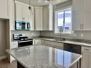 Kitchen featuring appliances with stainless steel finishes, light stone countertops, white cabinets, pendant lighting, and a center island