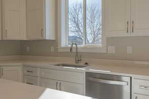 Kitchen featuring white cabinetry, stainless steel dishwasher, and light stone counters