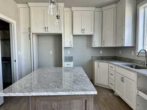 Kitchen with light stone countertops, pendant lighting, white cabinets, dark wood finished floors, and a kitchen island