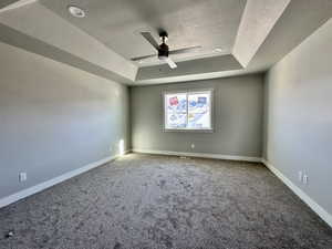 Unfurnished room featuring a tray ceiling, a textured ceiling, carpet floors, and ceiling fan