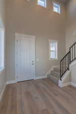 Entryway featuring healthy amount of natural light, stairs, a towering ceiling, and wood finished floors