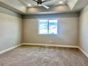 Carpeted spare room with a tray ceiling and a ceiling fan