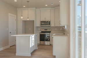 Kitchen featuring stainless steel appliances, white cabinetry, decorative light fixtures, a center island, and recessed lighting