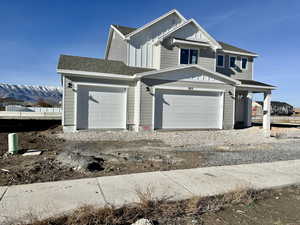 View of front facade featuring board and batten siding, roof with shingles, a mountain view, driveway, and an attached garage