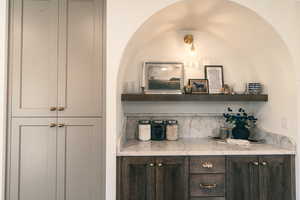 Bar featuring open shelves, dark brown cabinetry, and light stone countertops