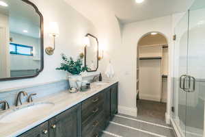 Full bathroom featuring double vanity, a shower stall, a spacious closet, recessed lighting, and dark tile patterned floors