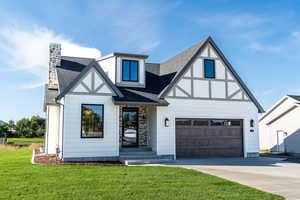 Tudor home with roof with shingles, concrete driveway, a front lawn, a chimney, and stone siding