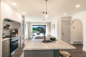 Kitchen with gray cabinetry, arched walkways, electric range, a kitchen island with sink, and recessed lighting