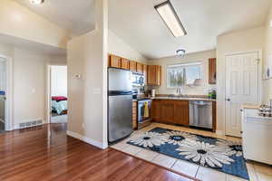 Kitchen with vaulted ceiling, brown cabinets, stainless steel appliances, light countertops, and light wood finished floors
