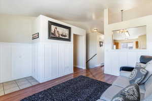 Living area with a decorative wall, light wood-style floors, a wainscoted wall, vaulted ceiling, and a chandelier