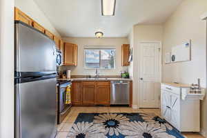 Kitchen with stainless steel appliances, light tile patterned floors, brown cabinets, and light countertops