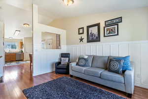 Living area featuring vaulted ceiling, wood finished floors, a decorative wall, and a wainscoted wall