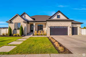 View of front of home with covered porch, stone siding, driveway, and a shingled roof