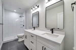 Bathroom with double vanity, dark tile patterned floors, tiled shower, and recessed lighting